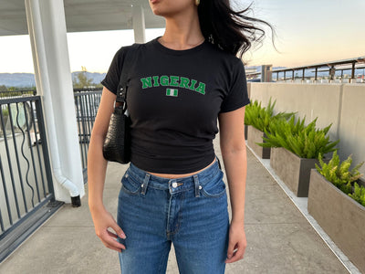 Black baby tee with arched green Nigeria lettering and small Nigerian flag graphic