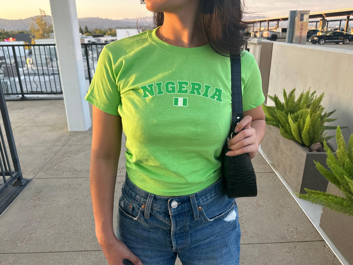 Black baby tee with arched green Nigeria lettering and small Nigerian flag graphic