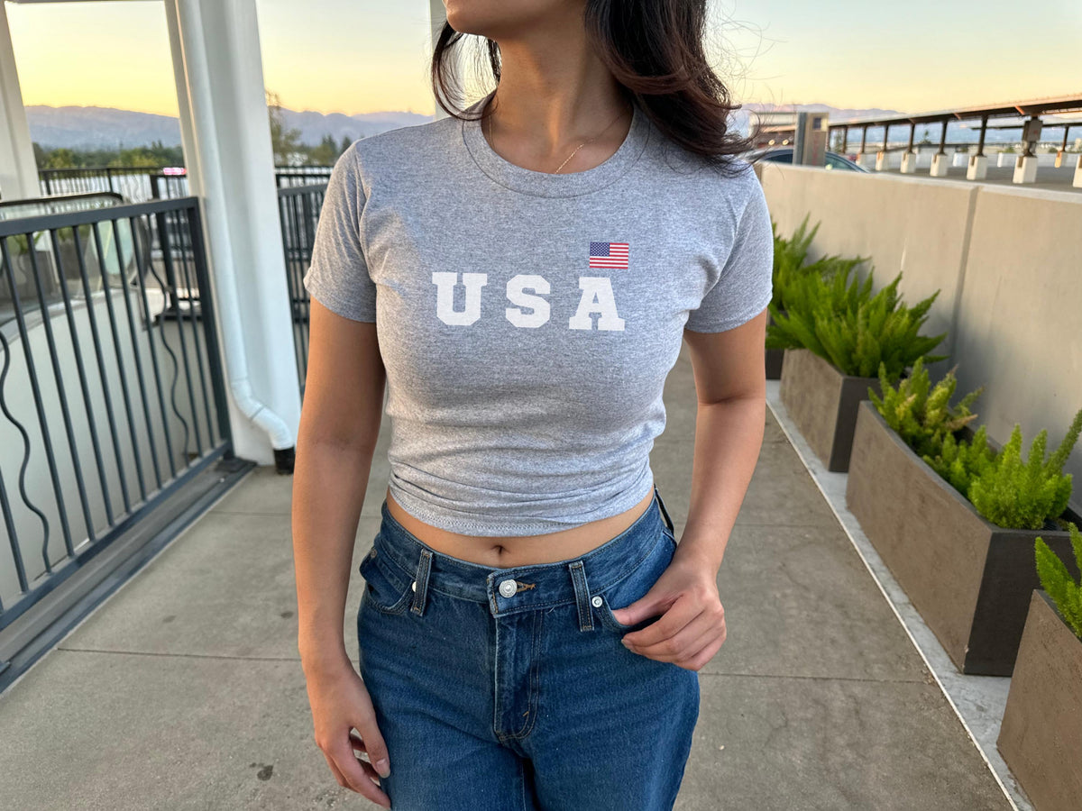 Navy fitted baby tee with bold USA lettering and small American flag graphic
