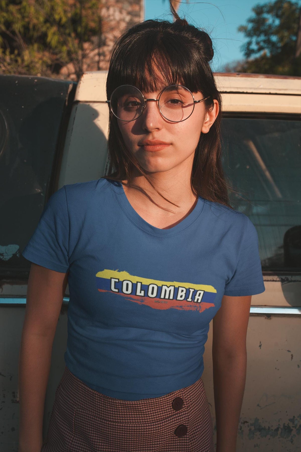 White baby tee with Colombia wordmark over yellow, blue, and red flag brush stroke design