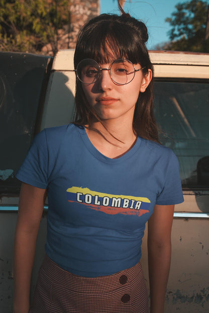 White baby tee with Colombia wordmark over yellow, blue, and red flag brush stroke design