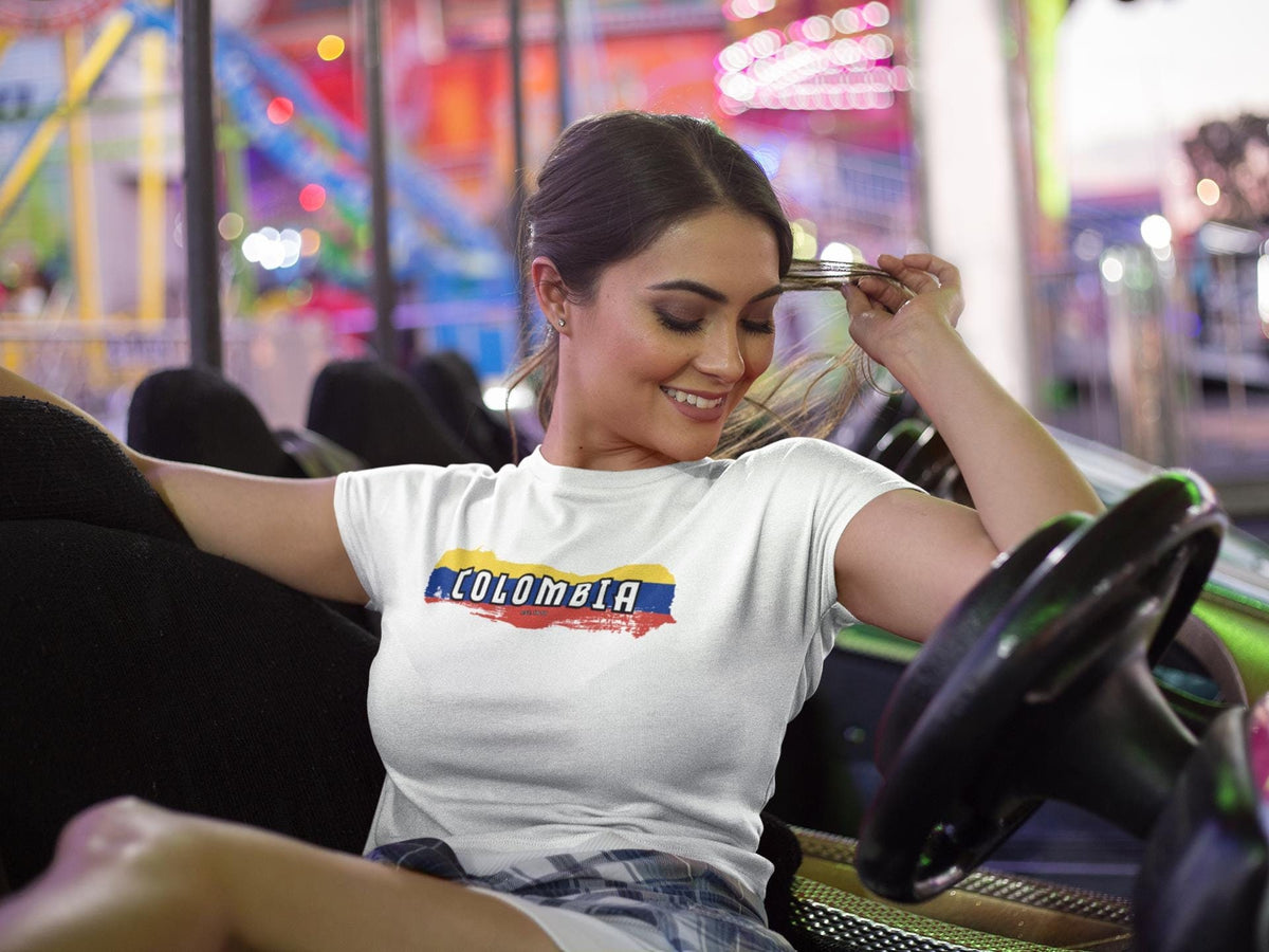 White baby tee with Colombia wordmark over yellow, blue, and red flag brush stroke design