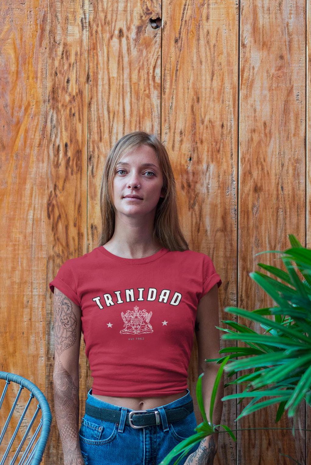 Red fitted baby tee with arched TRINIDAD text, coat of arms graphic, stars, and est 1962 detail.