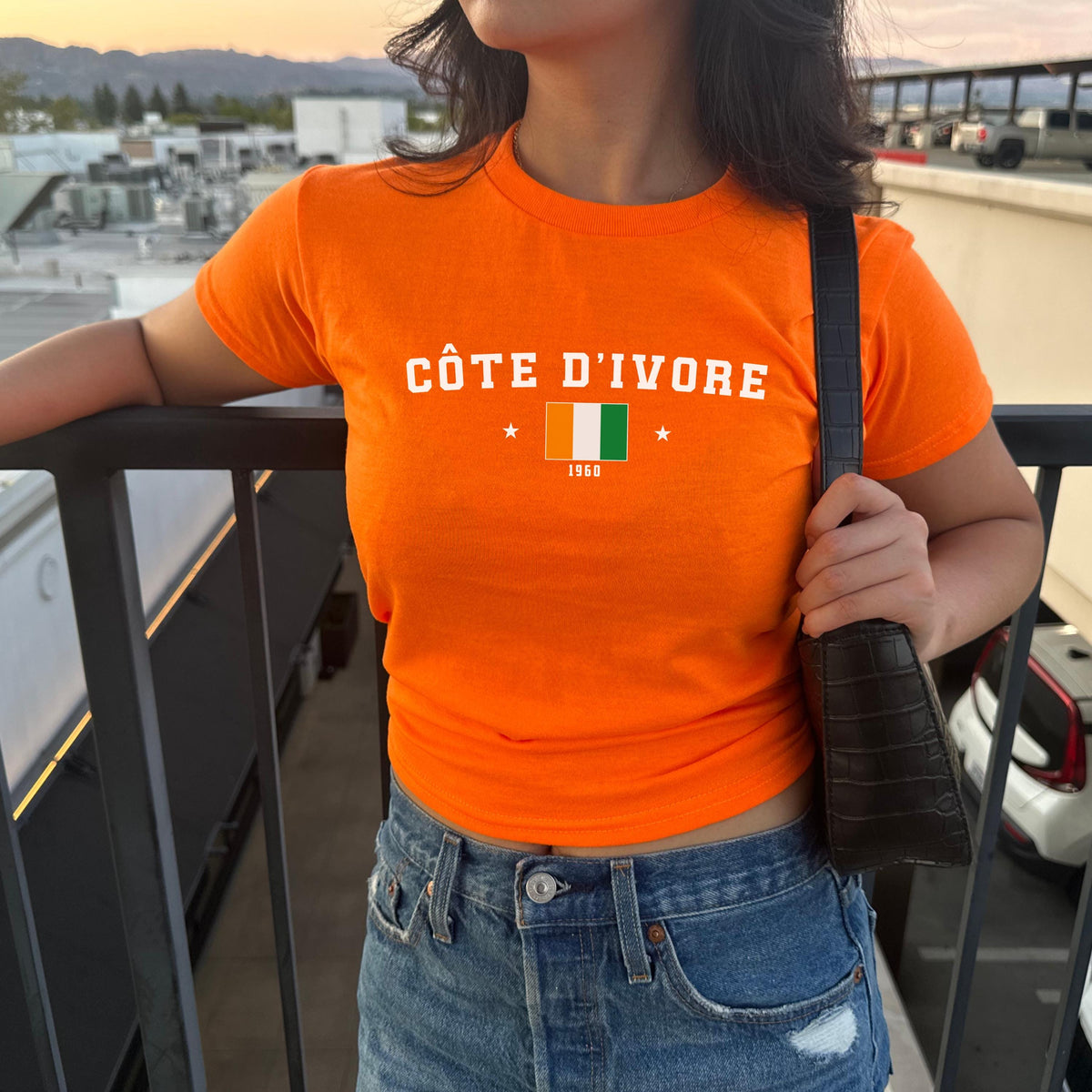 Orange baby tee with Côte d'Ivoire text, flag graphic, stars, and 1960 detail
