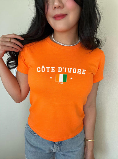 Orange baby tee with Côte d'Ivoire text, flag graphic, stars, and 1960 detail