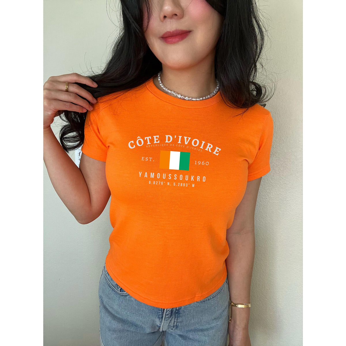 Orange baby tee with Côte d'Ivoire flag, Est. 1960, and Yamoussoukro text design.