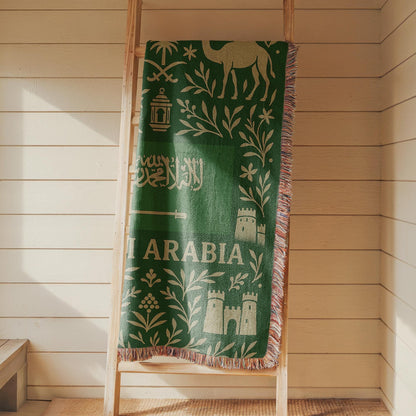 Green Saudi Arabia woven blanket with Arabic script, camel, palm trees, sword, lanterns, and fringe edges